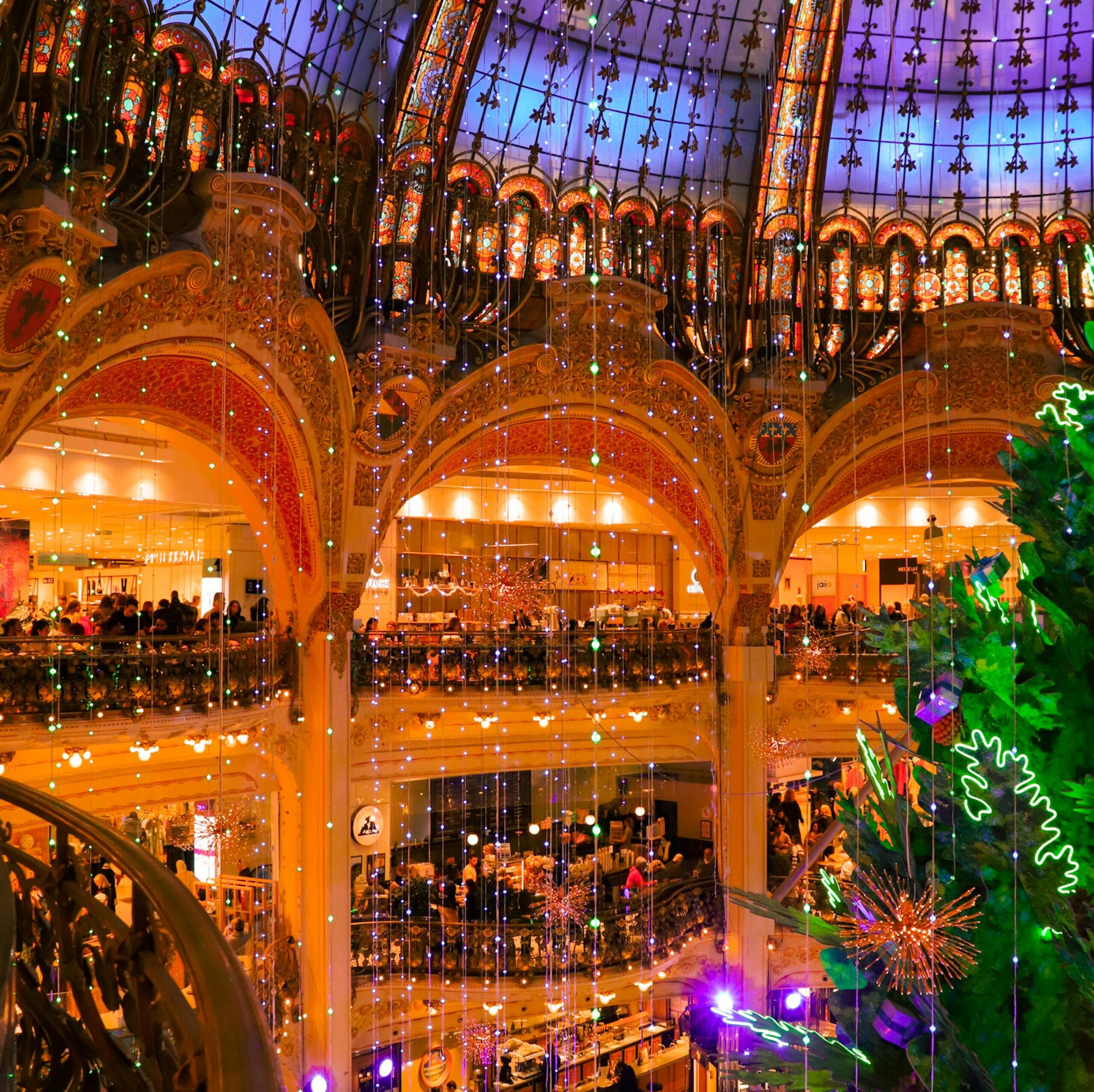 Illuminated view of a decorated Paris shopping mall interior during the holiday season.